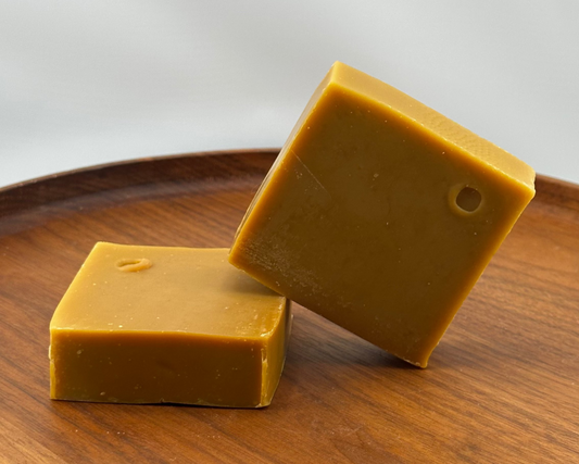 Two square carrot juice soap bars on a wooden board with a white background